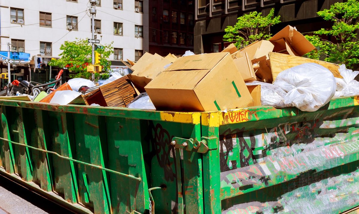 Open dumpster loaded with cardboard boxes and household junk for removal